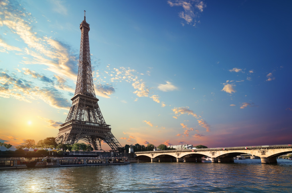 Eiffelturm in Paris bei Sonnenuntergang von der Seine aus gesehen. Eine beleuchtete Steinbogen-Brücke führt über den Fluss. Eiffelturm in Paris bei Sonnenuntergang von der Seine aus gesehen. Eine beleuchtete Steinbogen-Brücke führt über den Fluss.