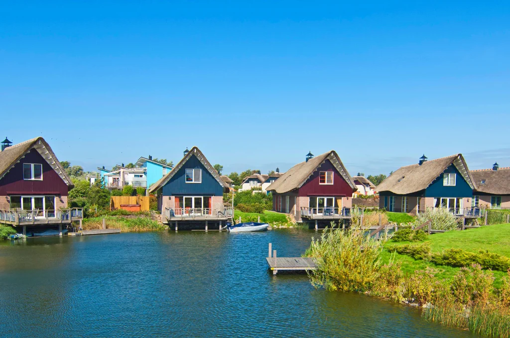 Gemini hat gesagt Eine Reihe von bunten Häusern mit Reetdächern am Ufer eines ruhigen Kanals an einem sonnigen Tag. Gemini hat gesagt Eine Reihe von bunten Häusern mit Reetdächern am Ufer eines ruhigen Kanals an einem sonnigen Tag.