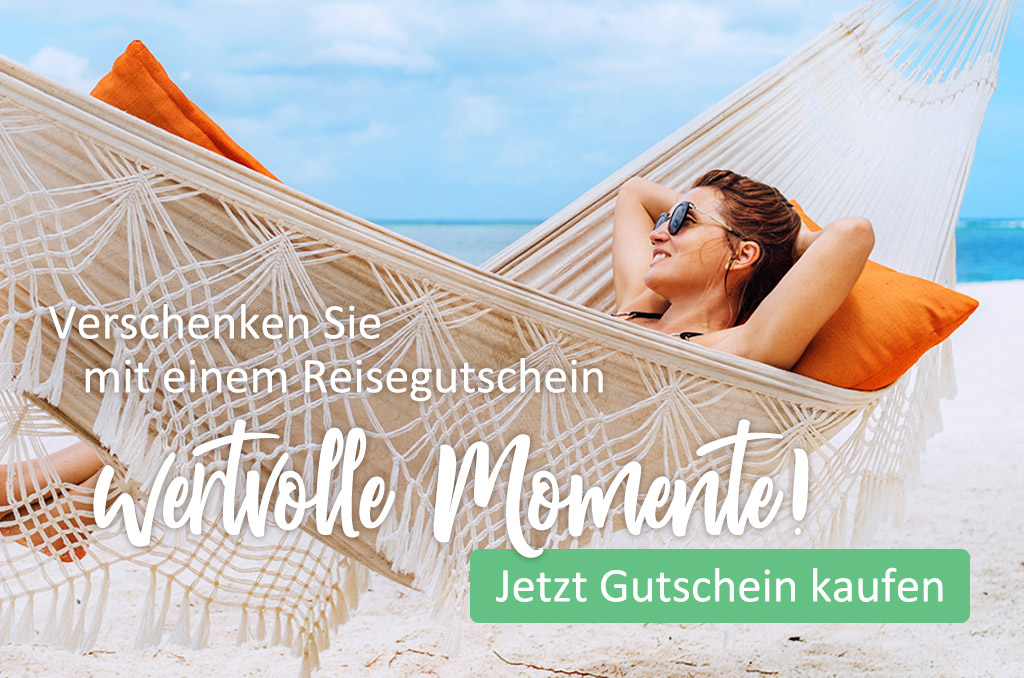 Eine Person entspannt sich in einer weißen Hängematte am Sandstrand, im Hintergrund das blaue Meer. Kaufen Sie einen Reisegutschein, um wertvolle Momente zu verschenken.