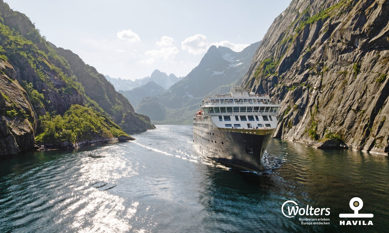 Ein Kreuzfahrtschiff fährt durch einen engen Fjord, umgeben von steilen Felswänden und grüner Vegetation. Im Hintergrund sind Berge unter einem leicht bewölkten Himmel. Ein Kreuzfahrtschiff fährt durch einen engen Fjord, umgeben von steilen Felswänden und grüner Vegetation. Im Hintergrund sind Berge unter einem leicht bewölkten Himmel.